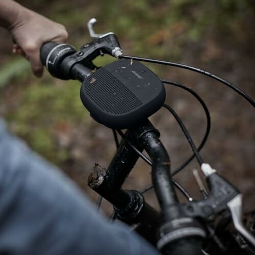 Person holding bicycle handlebar with speaker attached.