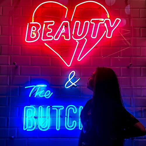 Neon sign reading 'Beauty & The Butch' with heart shape, silhouette of person in foreground.